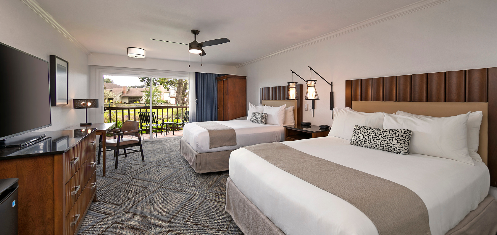 Hotel room with two queen beds, a desk, a balcony view, and modern decor, ready for guests.