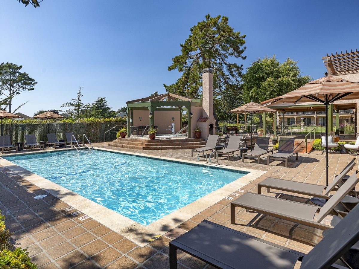 A sunny poolside scene with lounge chairs, umbrellas, and a relaxing outdoor seating area.