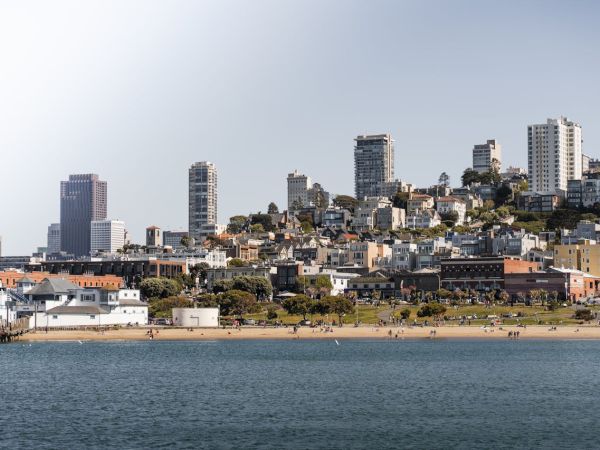 A coastal city with a sandy beach in the foreground and a mix of low houses and tall apartment buildings climbing up a hill by the water.