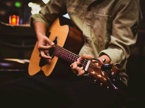 A person strums an acoustic guitar in a dim, cozy setting, focusing on the fretboard and picking hand, guitar in hand, night vibe.