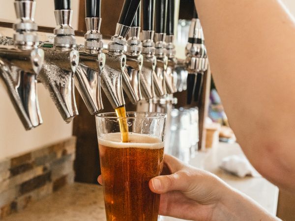 A bartender pours beer from multiple taps into a glass, hand steady as taps line up against a tiled bar.