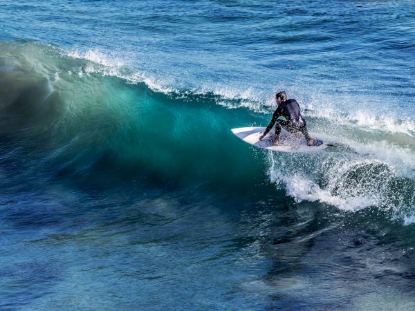 Surfer riding a turquoise wave on a board, gliding along the crest as the ocean churns around.