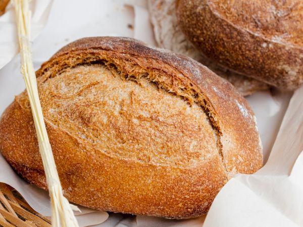 Fresh baked whole bread rolls with a crusty, golden crust resting on parchment, a wooden fork nearby for serving.