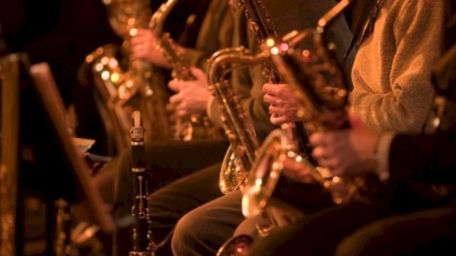 A row of musicians playing saxophones in a dimly lit concert setting, close-up on their brass instruments and hands, creating a warm jazzy vibe.