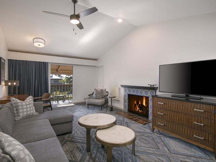 Cozy living room with a gray sectional, two nesting coffee tables, a stone fireplace, and a large flat-screen TV on a wooden dresser.