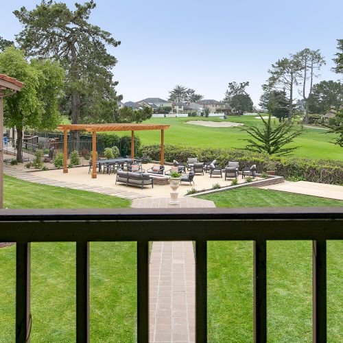 A well-kept backyard with a patio, outdoor seating, a pergola, and a lush green lawn extending to trees in the distance.