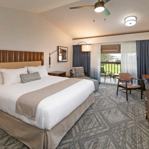 A hotel room with a king bed, nightstands, seating area, work desk, and large window with blue curtains. Top it at 140 characters, ending the sentence.