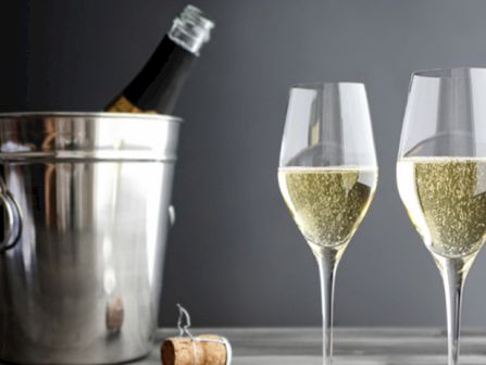 Champagne bottle chilling in a metal ice bucket with two filled fluted glasses nearby, cork on the table, elegant celebration vibe.