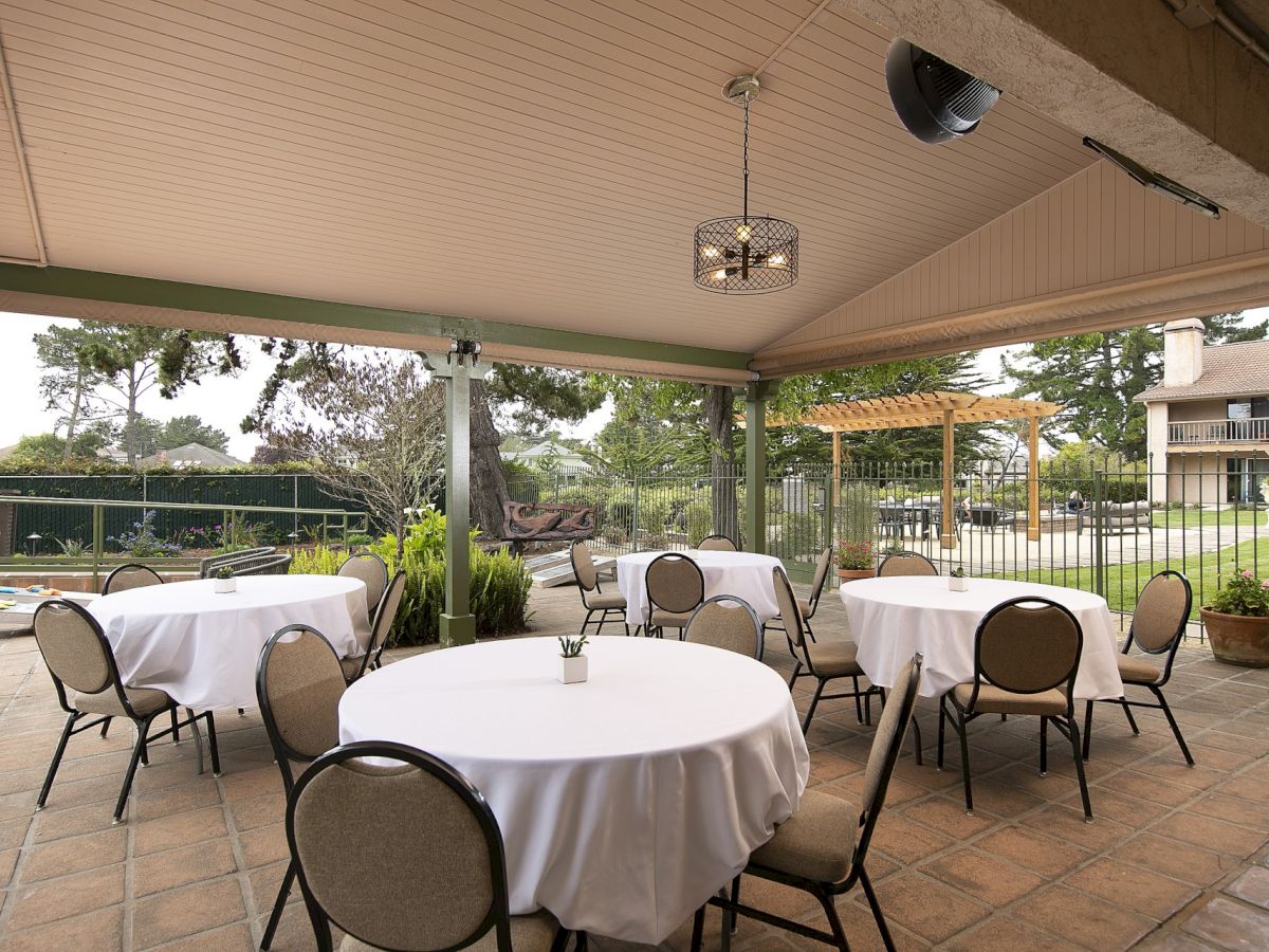 Outdoor restaurant patio with round tables, white tablecloths, and beige chairs under a covered area; looks ready for guests to dine.